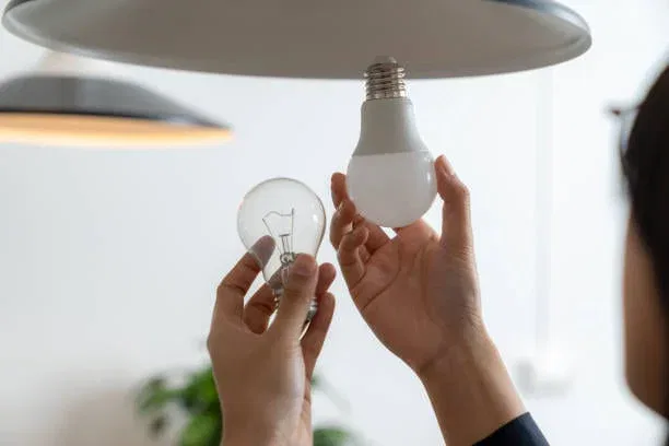 Hands replacing an incandescent bulb with an LED bulb in a ceiling light fixture in a home setting