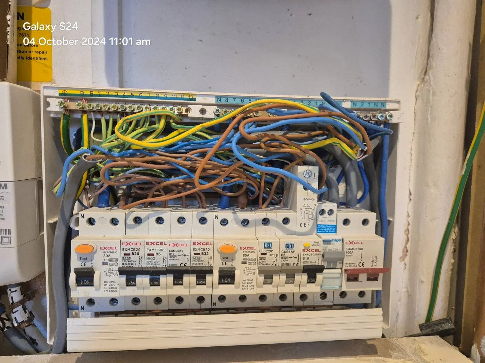 An open electrical fuse box showing multiple circuit breakers and a tangle of coloured wires. The photo is timestamped 04 October 2024 11:01 am in the top left corner. An open electrical fuse box showing multiple circuit breakers and a tangle of coloured wires. The photo is timestamped 04 October 2024 11:01 am in the top left corner.