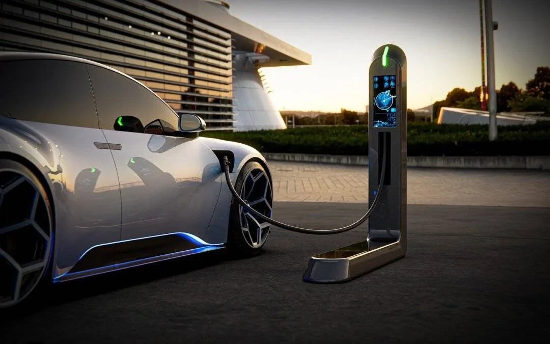 A sleek, modern electric car is parked and connected to a high-tech charging station outdoors near a contemporary building at sunset.