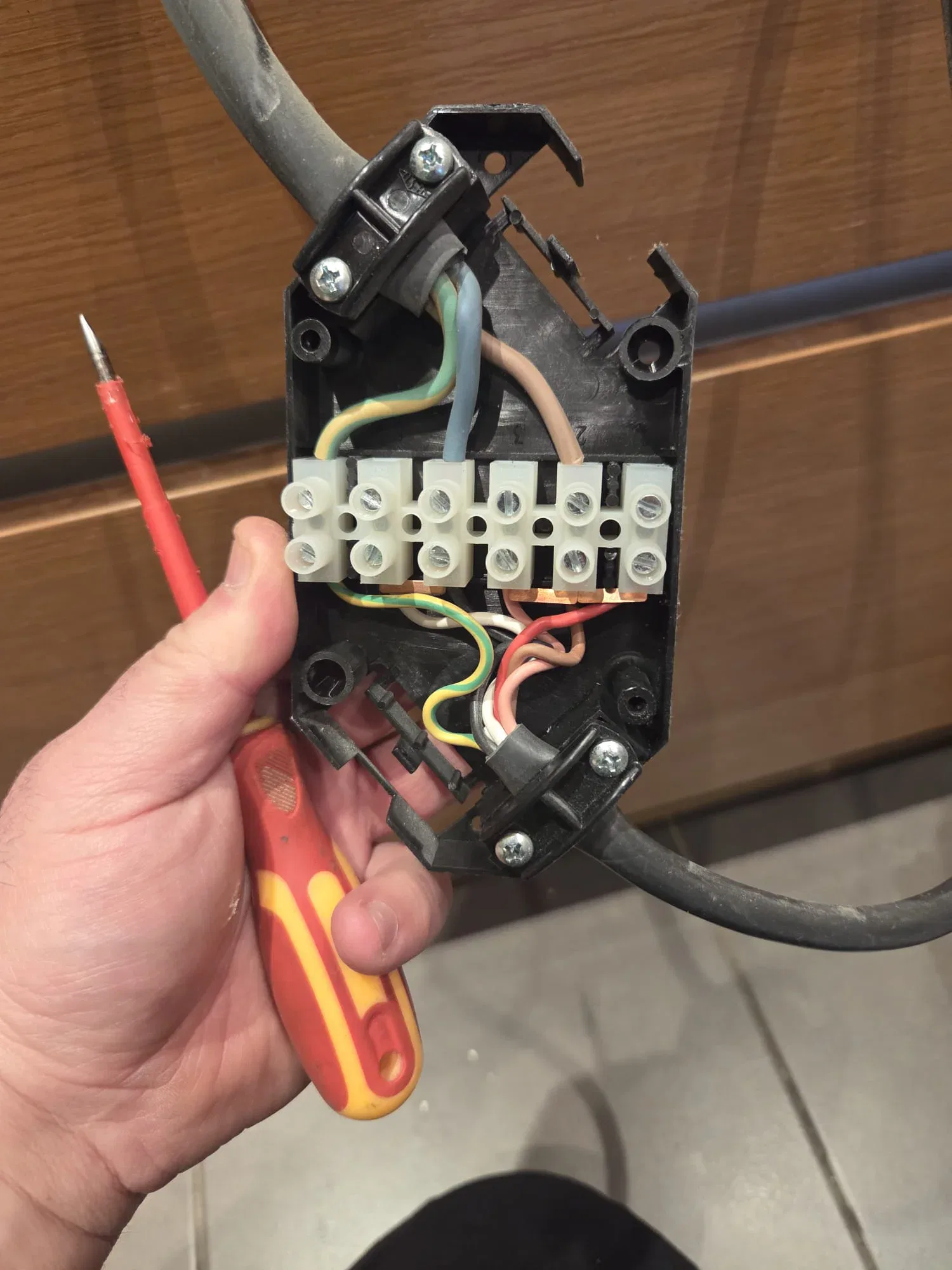 BuildSpark electrician London holding a disassembled electrical junction box with coloured wires and a screwdriver during inspection.