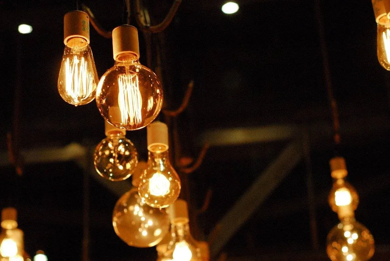 A close-up of several vintage-style incandescent light bulbs hanging from the ceiling, glowing warmly against a dark background.