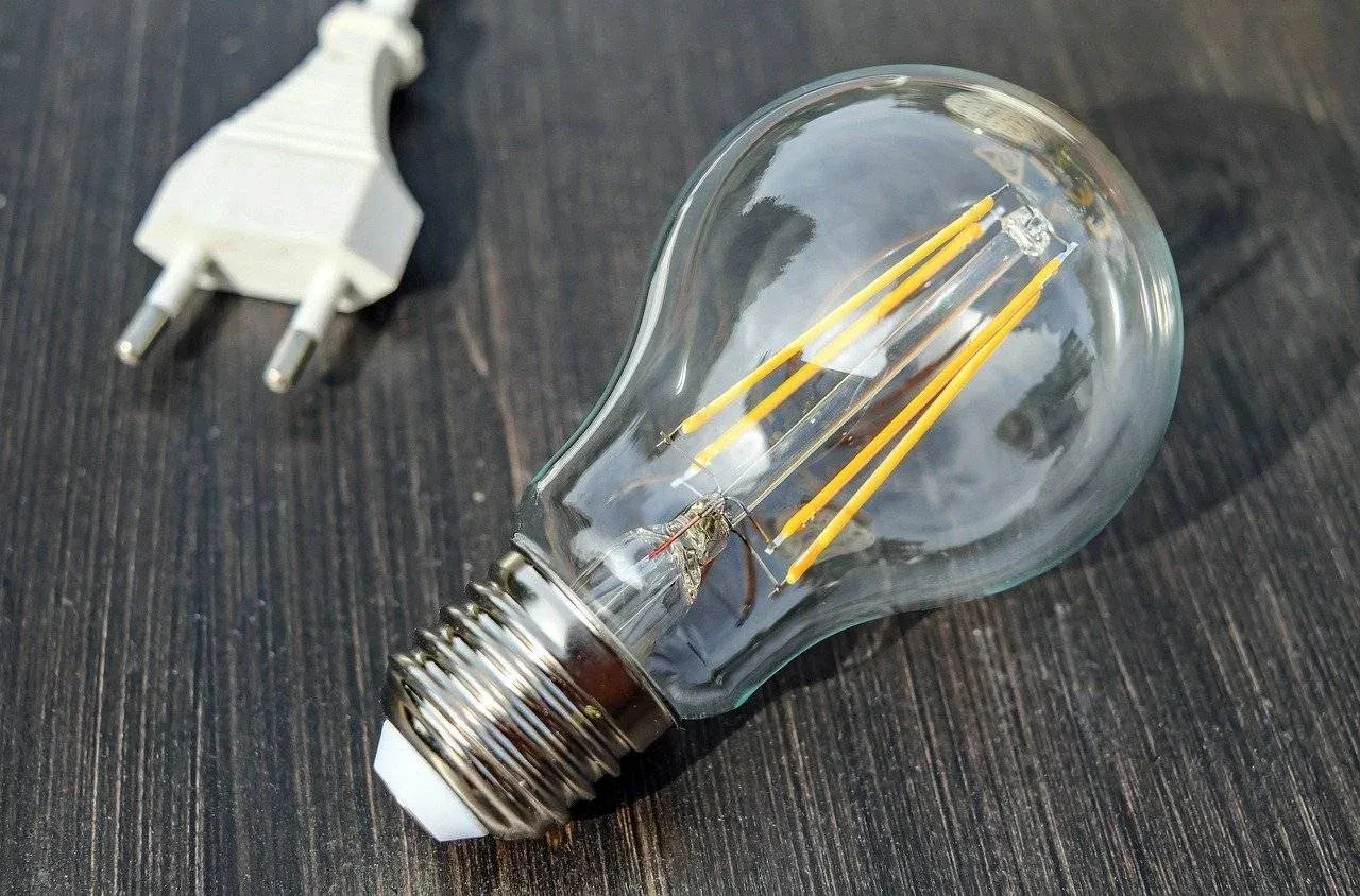 Electrician Tooting A clear LED light bulb lies on a dark wooden surface next to a white electrical plug.