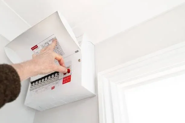 A person’s hand is pressing a switch on a household electrical fuse box, highlighting the need for urgent electrical repairs that a 24/7 electrician South West London can handle efficiently. A person’s hand is pressing a switch on a household electrical fuse box, highlighting the need for urgent electrical repairs that a 24/7 electrician South West London can handle efficiently.