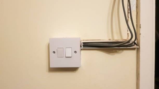 A white electrical light switch with exposed wires and an unfinished opening in the wall, highlighting untidy installation—ideal for a certified rewiring electrician or house rewiring Tooting project. A white electrical light switch with exposed wires and an unfinished opening in the wall, highlighting untidy installation—ideal for a certified rewiring electrician or house rewiring Tooting project.