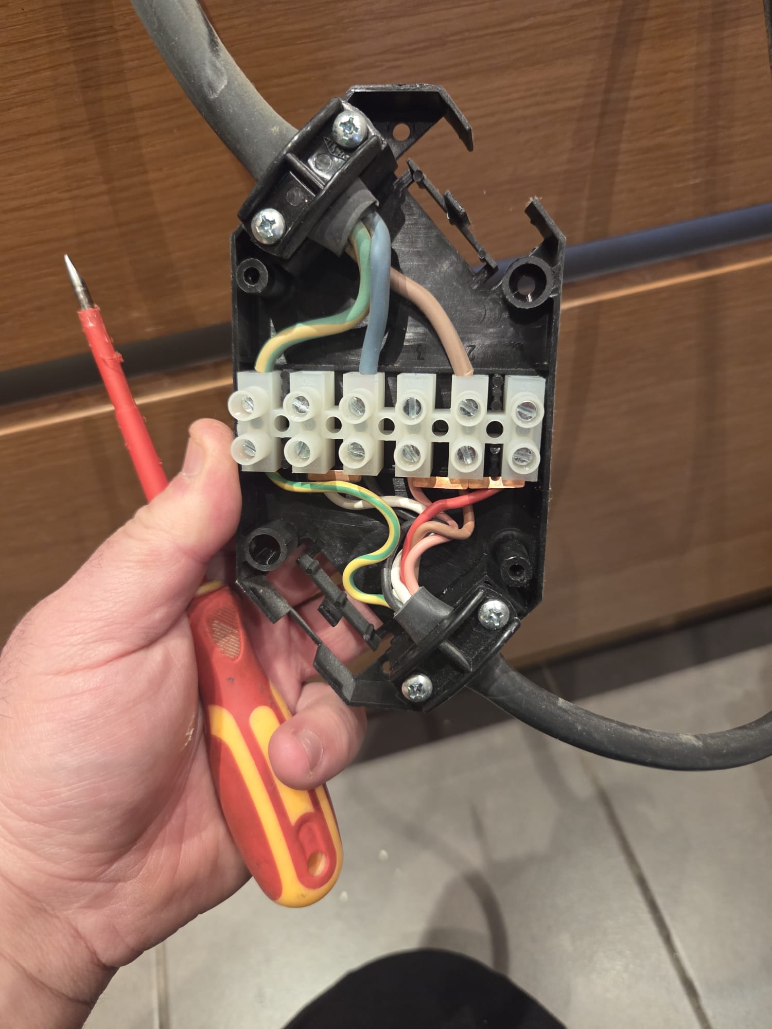 BuildSpark electrician London inspecting electrical junction box wiring BuildSpark electrician London holding a disassembled electrical junction box with coloured wires and a screwdriver during inspection.